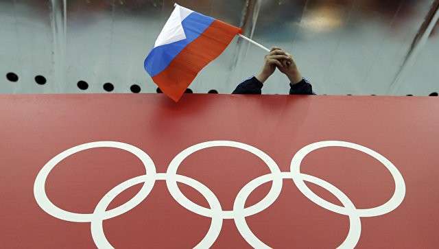 Болельщик держит российский флаг над логотипом олимпийских игр. Архивное фото Болельщик держит российский флаг над логотипом олимпийских игр. Архивное фото